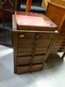 A narrow eleven-drawer wooden specimen cabinet with display glass top