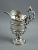 A HEAVY CIRCULAR BASED SILVER CREAM JUG, attractively decorated, having a mask spout and a handle in