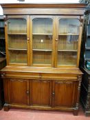 A VICTORIAN MAHOGANY THREE DOOR BOOKCASE having a shaped crown over twin glazed doors and central