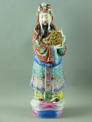 A CHINESE PORCELAIN STANDING FIGURE OF FORTUNE holding the calligraphy symbol for 'Blessed', the
