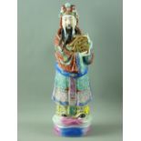 A CHINESE PORCELAIN STANDING FIGURE OF FORTUNE holding the calligraphy symbol for 'Blessed', the