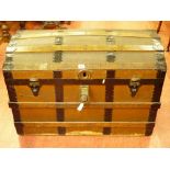 A VINTAGE DOME TOPPED TRAVEL TRUNK with wood and metal banding, leather carry handles marked 'M