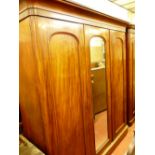 A VICTORIAN MAHOGANY TRIPLE WARDROBE having an inverted swept crown over a central mirrored door and