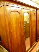 A VICTORIAN MAHOGANY TRIPLE WARDROBE having an inverted swept crown over a central mirrored door and