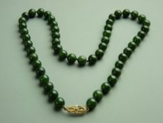 A DARK GREEN JADE BEAD NECKLACE, 50 cms with a nine carat gold bow and twist clasp