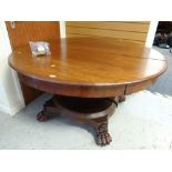 An antique circular two sectioned mahogany dining table with central support and lion claw feet