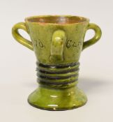 AN EWENNY POTTERY LOVING CUP in green glaze with three loop handles and with a ribbed waist,
