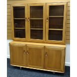 AN ERCOL BLONDE LOUNGE UNIT composed of a base with three cupboards and a top of three glazed