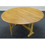 A GOOD ERCOL DROP LEAF OVAL DINING TABLE in blonde, both leaves folding to form a narrow practical