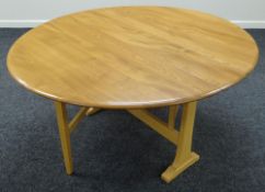 A GOOD ERCOL DROP LEAF OVAL DINING TABLE in blonde, both leaves folding to form a narrow practical