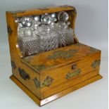 AN OAK THREE BOTTLE TANTALUS with front twin lid compartment and single drawer, brass mounted and