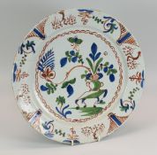 A DELFT TIN-GLAZED POTTERY CHARGER primitively painted in blue, green and red with a jardiniere on a