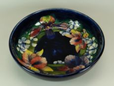 A MOORCROFT SHALLOW BOWL decorated in blue ground with a circling range of flowers, Walter Moorcroft