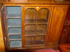 A LIGHT WOOD STANDING BOOKCASE having a centre six pane glazed door with cupboards either side, on