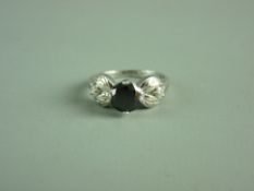 A NINE CARAT WHITE GOLD DRESS RING having a circular black diamond with a white diamond in a leaf