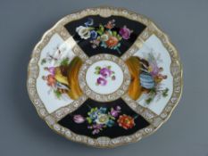 A CIRCULAR DRESDEN CHINA PLATE having a gilt scrolled border with four outer panels of alternating