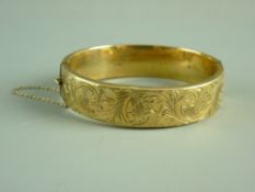 A NINE CARAT GOLD WIDE HOLLOW BANGLE with half bright cut decoration and safety chain, 20.7 grms (