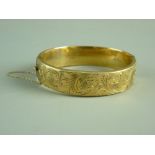 A NINE CARAT GOLD WIDE HOLLOW BANGLE with half bright cut decoration and safety chain, 20.7 grms (