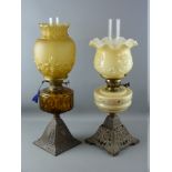 TWO VICTORIAN OIL LAMPS, both on iron bases, one with amber glass reservoir and similar coloured