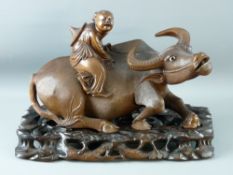 A CHINESE HARDWOOD CARVING on stand in the form of a recumbent water buffalo with a child upon its