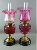 TWO VICTORIAN OIL LAMPS, both brass columned with cranberry glass shades and reservoirs, one