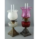 TWO VICTORIAN OIL LAMPS with iron bases, one with cranberry glass reservoir, the other clear