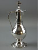 A CIRCULAR BASED NARROW NECKED SILVER COMMUNION JUG with globular body and hinged lid with prominent