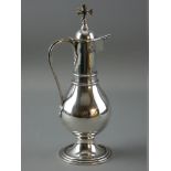 A CIRCULAR BASED NARROW NECKED SILVER COMMUNION JUG with globular body and hinged lid with prominent