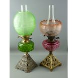 TWO VICTORIAN OIL LAMPS with iron bases, coloured glass reservoirs and fine etched glass shades