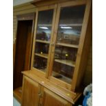 A pine bookcase cupboard with two-door glazed top & brass fittings