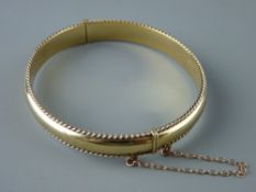 A NINE CARAT CLOGAU GOLD BANGLE with gadrooned edging and safety chain in original box, 13 grms
