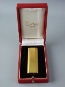 A CASED CARTIER YELLOW METAL CIGARETTE LIGHTER, no. A21161 and with neat hard cover Cartier