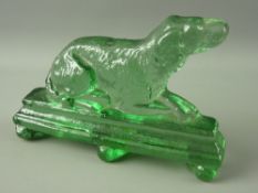 A RARE VICTORIAN GREEN GLASS DOORSTOP of a recumbent dog on a stepped base with three triangular