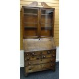 AN EARLY NINETEENTH CENTURY OAK BUREAU BOOKCASE having a two door glazed top with sloped front