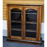 A TWO DOOR OAK & GLAZED BOOKCASE with carved detail to the shelves, base and borders, 115cms wide,
