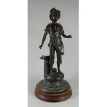 A BRONZE FIGURE OF A BLACKSMITH'S BOY standing aside an anvil on a circular base and wooden mount,