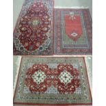 THREE SMALL RED GROUND WOVEN WOOLLEN EASTERN CARPETS, all having bordered edges and tasselled