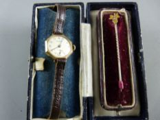 A NINE CARAT GOLD LADY'S WRISTWATCH with leather strap and a fifteen carat gold stick pin with small
