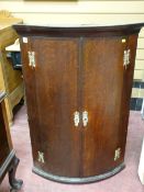 AN EARLY 19th CENTURY BOW FRONT HANGING WALL CUPBOARD in oak with crossbanded mahogany, eagle topped