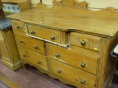 A VICTORIAN STRIPPED PINE SIDEBOARD having a carved rail back and shaped front top over an