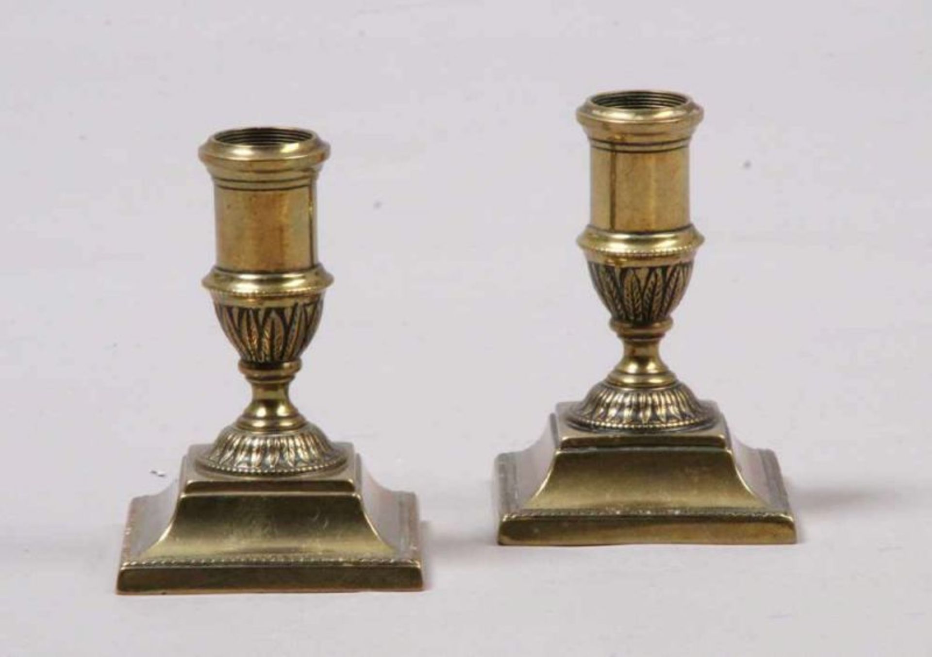 Paar Messingleuchter. Um 1900.Empirestil. Quadratischer Sockel, reliefierter Schaft. H: 11 cm. 20.00