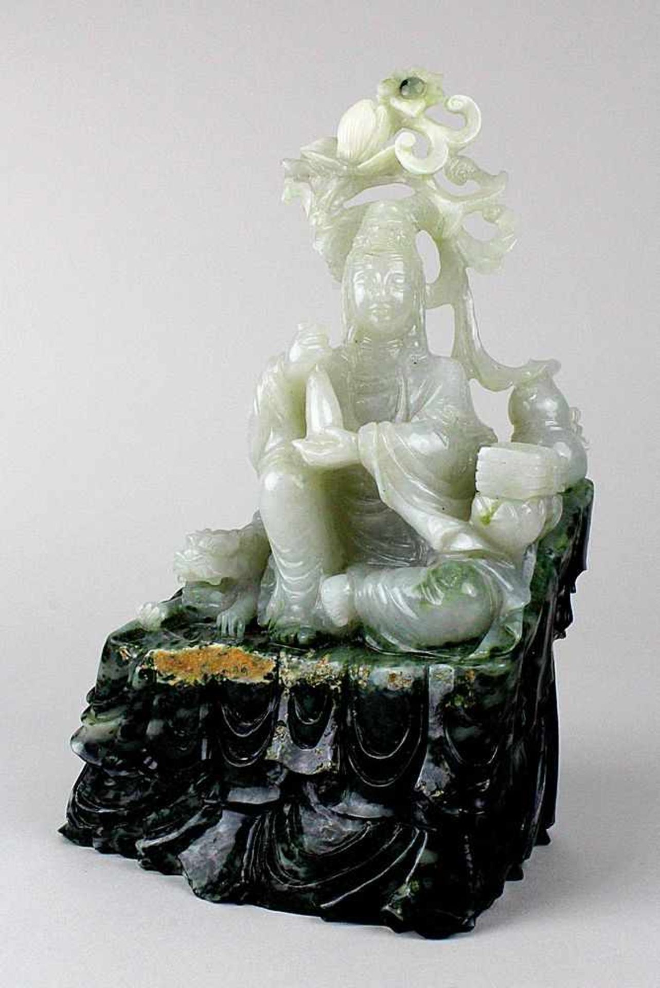 Guanyin, China um 1900. Sitzende Figur mit Fohund und Attributen aus hellgrüner Jade mit