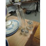 A tall glass perfume bottle with white metal lid and similar cruet set