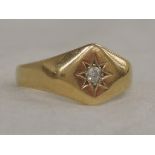 A yellow metal signet ring stamped 18ct having a diamond insert in a star burst setting
