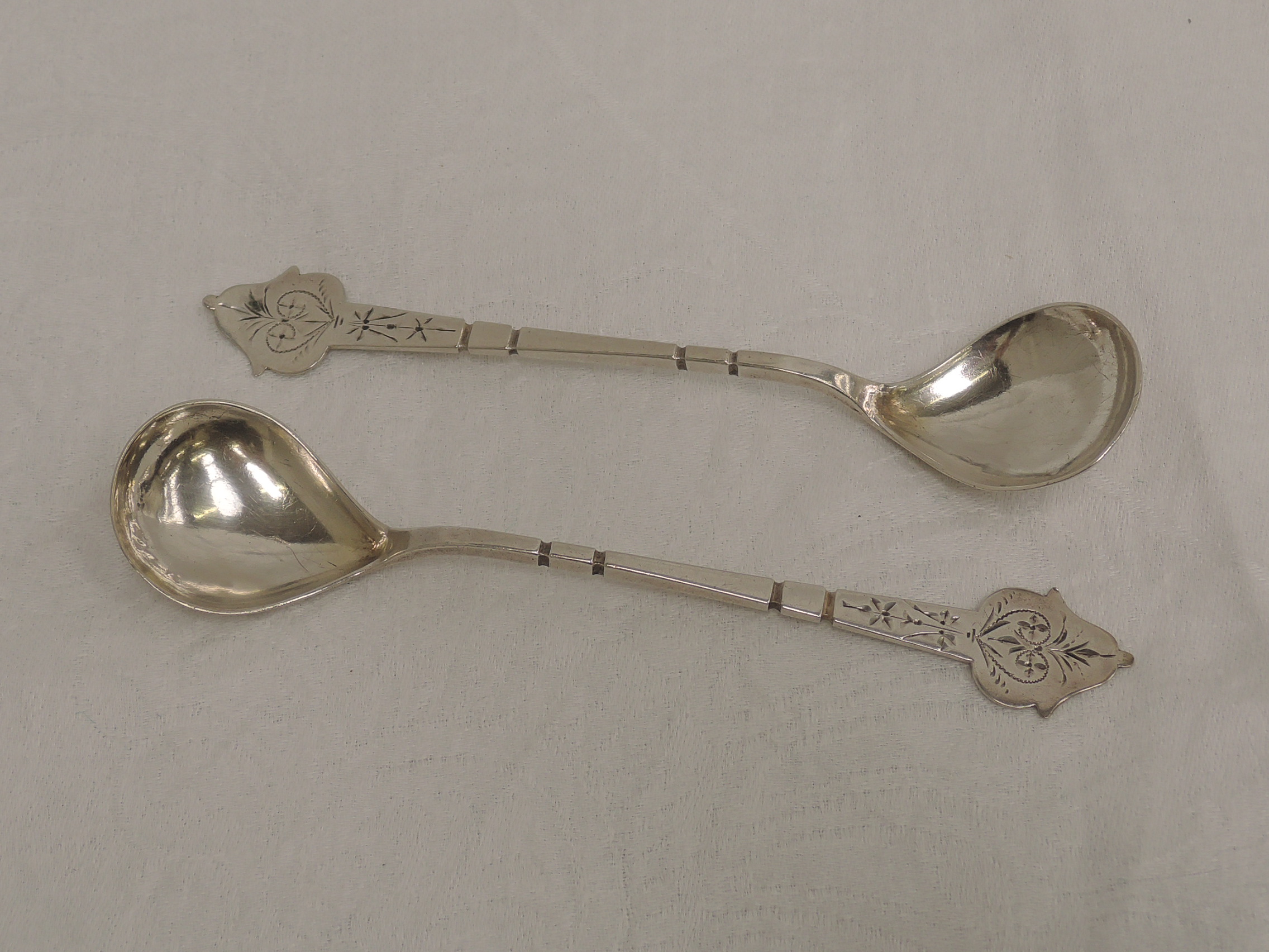 A pair of white metal spoons, possibly Danish having bright cut engraving to decorative terminals