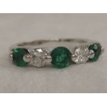 A lady's half eternity ring having three emeralds interspersed by two diamonds in a raised collar
