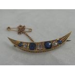 A Victorian yellow metal crescent brooch stamped 15ct having four graduated sapphires interspersed