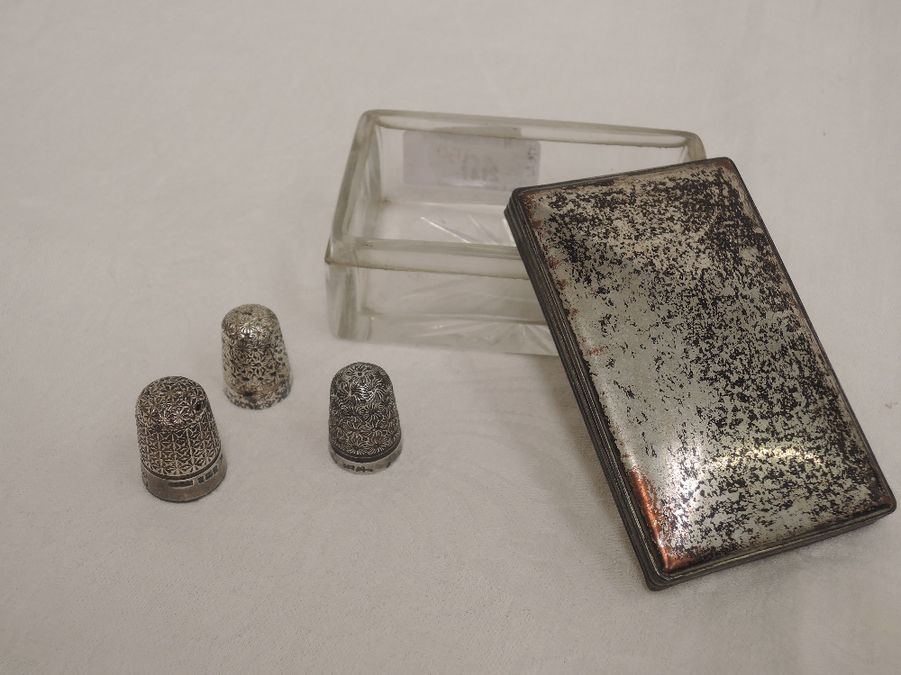 A glass and white metal dressing table box containing three HM silver and white metal thimbles