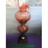 An early 20th century cast base oil lamp having cranberry glass reservoir and fluted shade