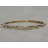 A yellow metal hinged bangle stamped 14K having 33 diamonds, approx .66ct in a channel setting
